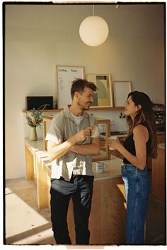 a man standing next to a woman holding a cup in her hand and looking at each other