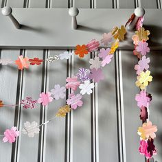 some paper flowers are hanging from a metal rack on the wall with clothes pins attached to it