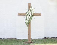 a wooden cross with flowers on it in front of a white brick wall and grass