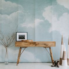 a wooden desk sitting in front of a wall with clouds painted on it and two vases next to it