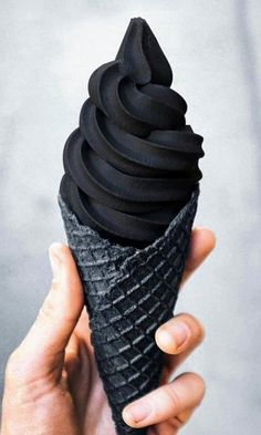 a hand holding an ice cream cone with black icing on it's tip