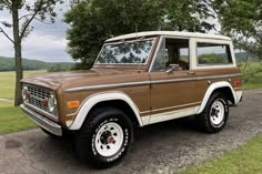 an old ford bronco is parked on the side of the road in front of some trees