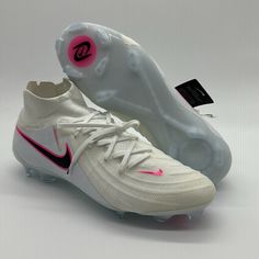 a pair of white and pink nike soccer cleats on a gray background with a black tag