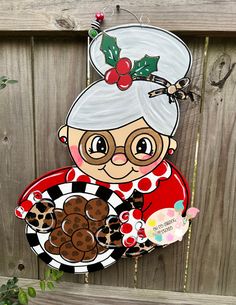 an old lady holding a plate with cookies and holly on it, hanging from a wooden fence