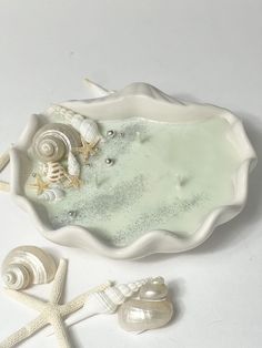 shells and seashells in a bowl on a white surface with starfish nearby