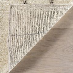 a close up view of the corner of a rug on a wooden floor with white and gray tones