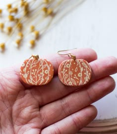 small orange and white painted pumpkin earrings on a person's hand