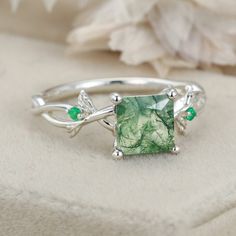 a close up of a ring with a green stone in the middle and leaves around it