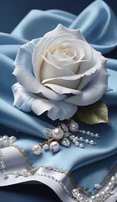 a white rose sitting on top of a blue satin covered table cloth next to pearls