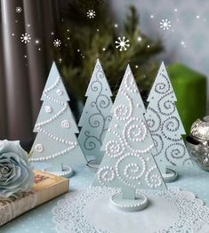 three small christmas trees sitting on top of a table next to a book and candle