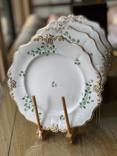 four white plates with green designs on them sitting on a wooden table in front of a window