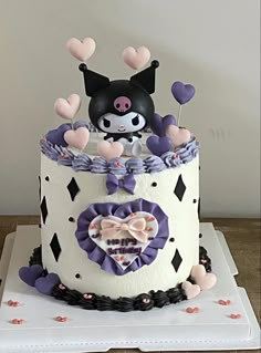 a white and purple cake decorated with an animal on it's top, surrounded by hearts