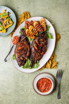 grilled meat and vegetables on a white plate next to a small bowl of sauce