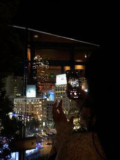 a woman taking a photo with her cell phone at night in front of a cityscape