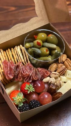 an open box filled with assorted food on top of a wooden table next to a bowl of fruit and crackers