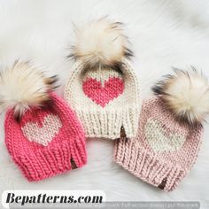 three knitted hats with hearts and pom - poms on white furnishing