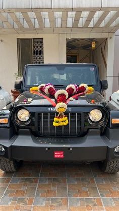 a jeep decorated with flowers and garlands in front of a car parked on the street