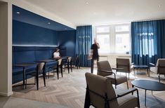 a room with chairs, tables and people standing in the doorway to another room that has blue curtains