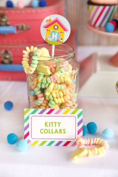 a jar filled with colorful candy sitting on top of a table next to cupcakes