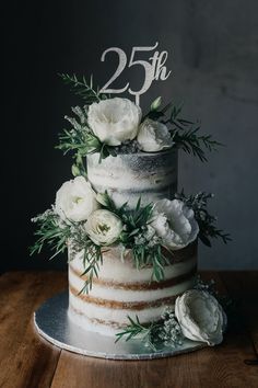 a wedding cake with white flowers and greenery on the top is decorated with a 25th sign