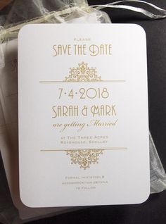 a white and gold save the date card on top of a plastic bag with ribbon