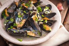 a white bowl filled with mussels on top of a wooden table