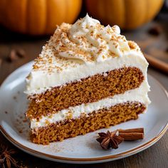 a slice of carrot cake on a plate with cinnamon sticks and pumpkins in the background