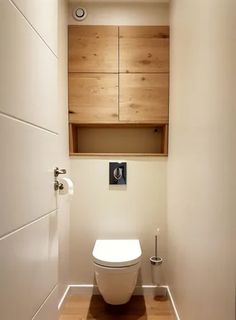 a white toilet sitting inside of a bathroom next to a wooden cabinet above it's door