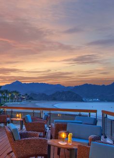 an outdoor dining area with wicker furniture and candles on the table at dusk overlooking water