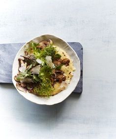 a white bowl filled with lots of food on top of a blue table cloth next to a knife