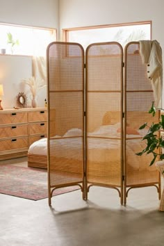 a room divider made out of bamboo with a plant in the foreground and a bed behind it