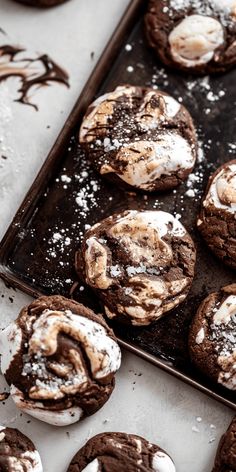 chocolate cookies covered in powdered sugar sit on a baking tray next to other baked goods