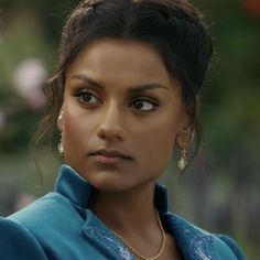 a close up of a person wearing jewelry and looking at the camera with a serious look on her face