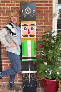 a woman standing next to a wooden nutcracker on the front porch with potted plants