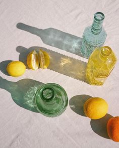 three lemons, two oranges and one green bottle on a white tablecloth