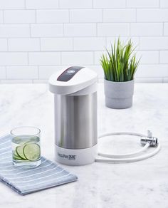 an electric juicer sitting on top of a counter next to a glass and potted plant