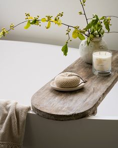 a wooden table topped with a candle next to a white vase filled with green leaves