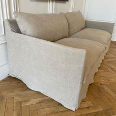 a beige couch sitting on top of a hard wood floor next to a white wall