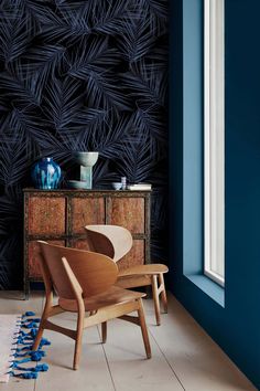 a chair and table in front of a blue wall with black leaves on it's side