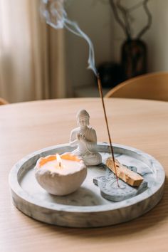 a small buddha statue sitting on top of a wooden table next to a white bowl