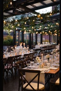 the tables are set for an event with white flowers and greenery hanging from the ceiling