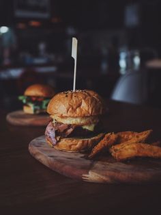 two burgers and some fried chicken on a wooden board with a toothpick in the middle