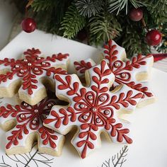 several decorated cookies on a white plate next to a christmas tree with red and silver decorations