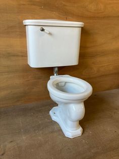 a white toilet sitting on top of a wooden floor next to a wood paneled wall