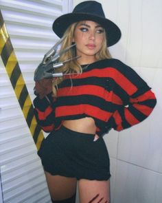 a woman wearing a black hat and red striped shirt holding a pair of scissors in her right hand