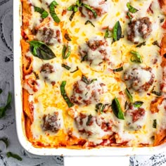 a casserole dish with meatballs, cheese and spinach leaves on top