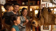 a group of people petting a sloth hanging from a wooden rail in a living room