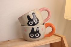 two mugs with faces painted on them are sitting on a shelf next to a lamp