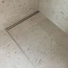 the corner of a shower stall in a tiled floored area with a drain running through it