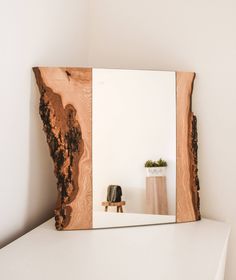 a wooden mirror sitting on top of a white shelf next to a vase and potted plant